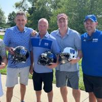 Five football alums holding football helmets on the course.